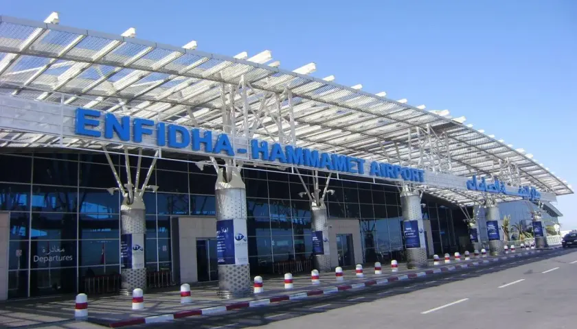 Nowoczesny budynek lotniska Enfidha-Hammamet w Tunezji, z niebieskimi literami nazwy i szklaną fasadą.