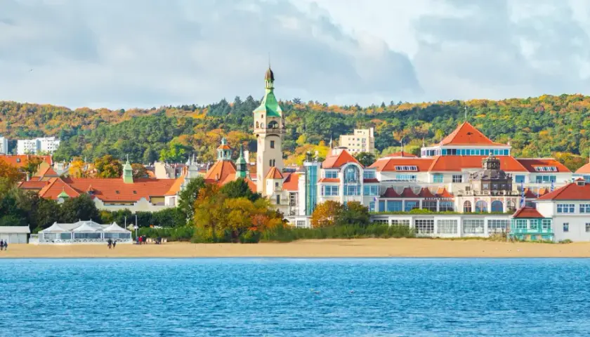 Malownicze widoki na plażę i zabytkowe budynki w Sopocie. Zobacz słynną latarnię morską i kościół na tle jesiennych drzew.