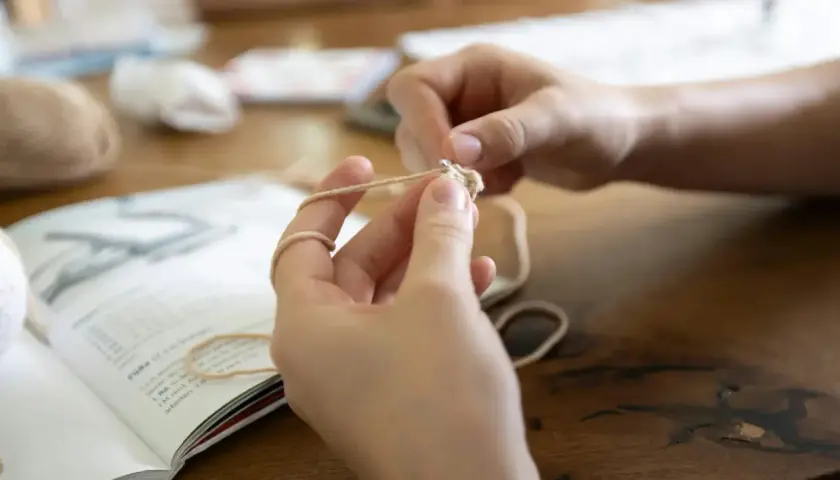 Mani che imparano il lavoro a maglia per principianti, seguendo un libro di istruzioni.