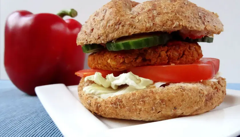 Pyszny burger z ciecierzycy z pomidorem, sałatą i ogórkiem, obok czerwona papryka.