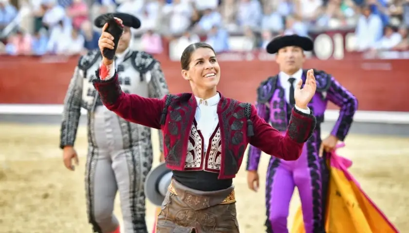 Mujeres de toreros famosos, con trajes de luces, saludan al público en la plaza de toros.