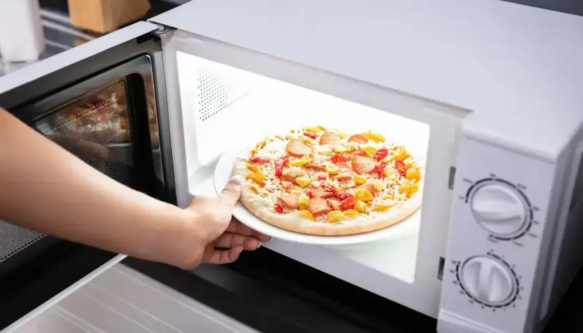 Ręka wkłada mrożoną pizzę do mikrofali. Czy mrożona pizza nadaje się do mikrofali? Zobaczmy!