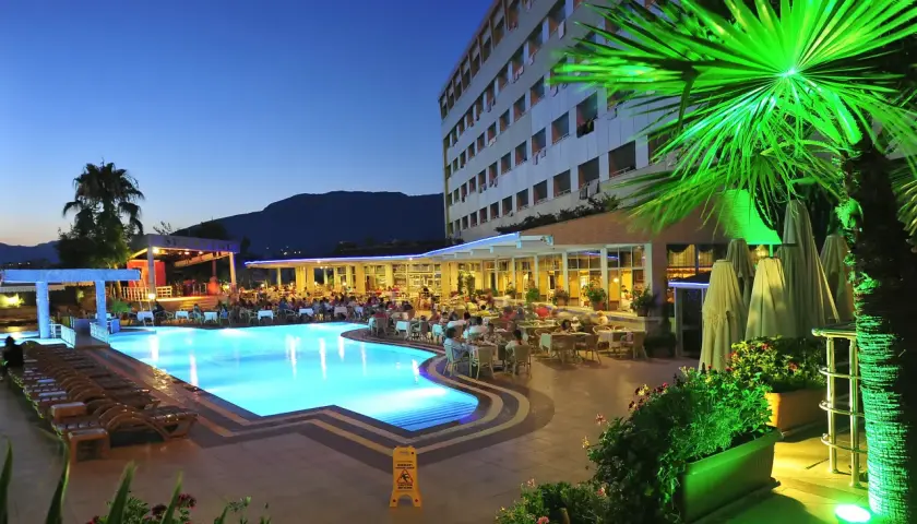 Wieczorny relaks przy basenie w Kirbiyik Resort Hotel. Goście siedzą przy stolikach, a basen lśni błękitem.