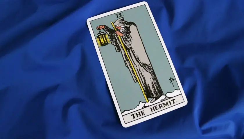 Karta Tarota "Pustelnik" (The Hermit) na niebieskim tle. Symbolizuje introspekcję, mądrość i poszukiwanie wewnętrznego światła.