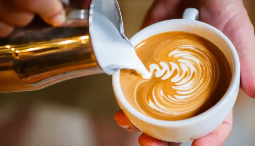Barista tworzy latte art, wlewając spienione mleko do kawy. Idealne mleko do cappuccino to podstawa pięknego wzoru.