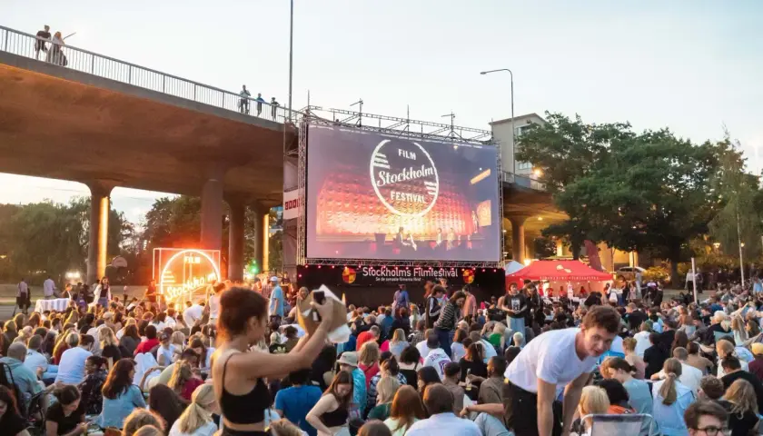 Stor publik samlad för utomhusbio under Stockholms Filmfestival. En stor duk visar festivalens logotyp.