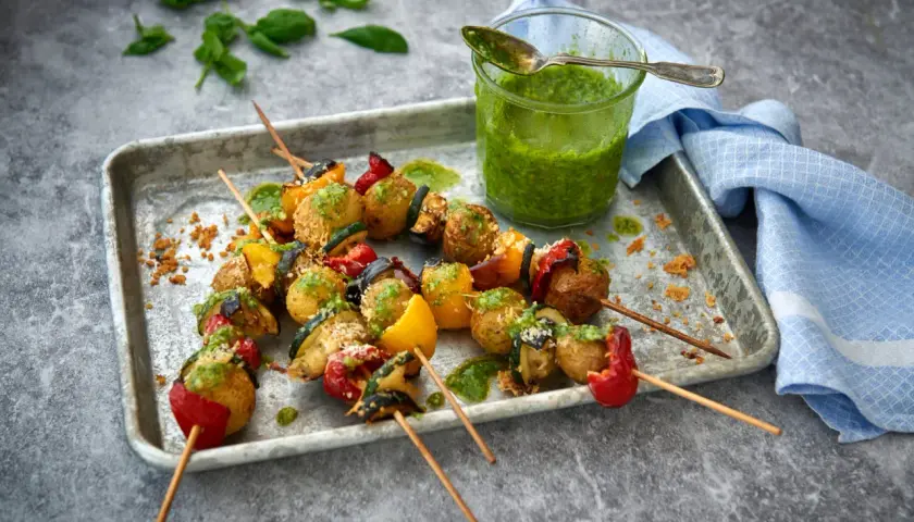 Grillade vegetariska grillspett med potatis, paprika och zucchini, serverade med en grön sås.