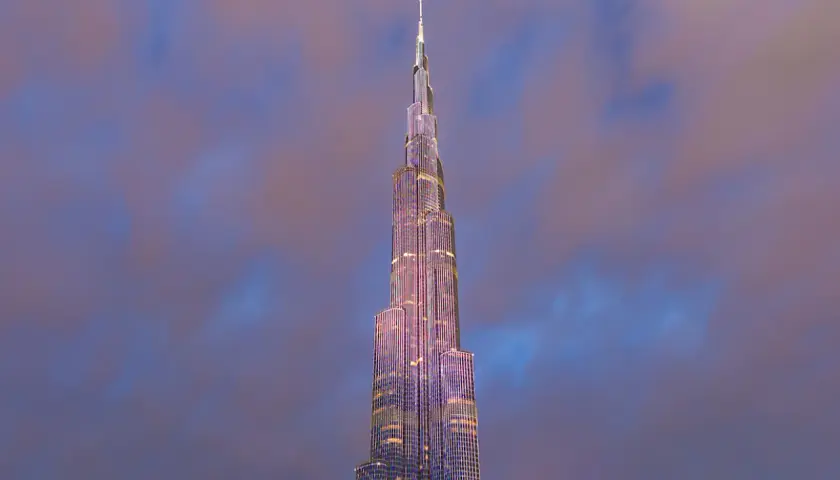 Burj Khalifa oświetlony na fioletowo na tle zachmurzonego nieba.