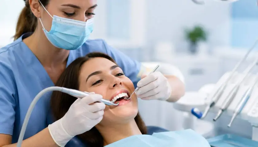 Dentista esegue pulizia dei denti. La paziente sorride, nonostante la paura che la pulizia dei denti fa male.