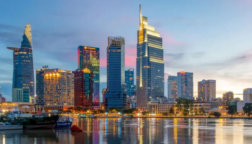 Ho Chi Minh Miasto nocą, z lśniącymi wieżowcami odbijającymi się w wodzie.
