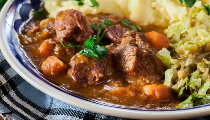 Un plat réconfortant de navarin d'agneau, avec des morceaux de viande tendres, des carottes et une sauce savoureuse, servi avec de la purée et du chou. Une recette parfaite pour un repas familial.