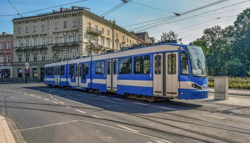 Niebiesko-biały tramwaj na torach w Krakowie. To część krakowskiej komunikacji miejskiej, która przewozi pasażerów przez miasto.
