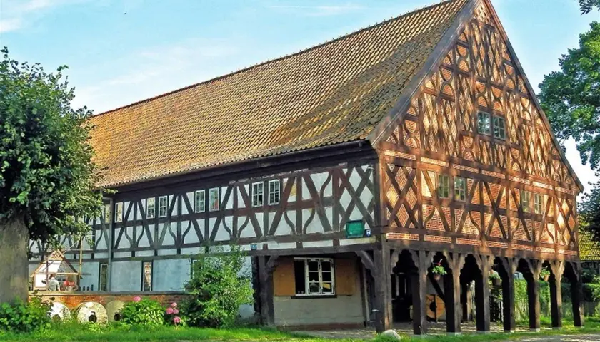Drewniany dom podcieniowy, część szlaku mennonitów, z charakterystyczną kratownicą i ceramicznym dachem.