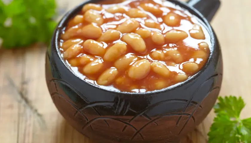 Un bol en terre cuite rempli de haricot blanc en sauce tomate, garni de persil frais sur fond de bois.
