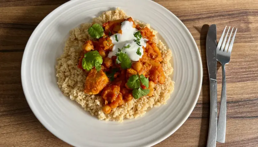 Tagine z kurczakiem i ciecierzycą na kuskusie, udekorowane jogurtem i kolendrą.
