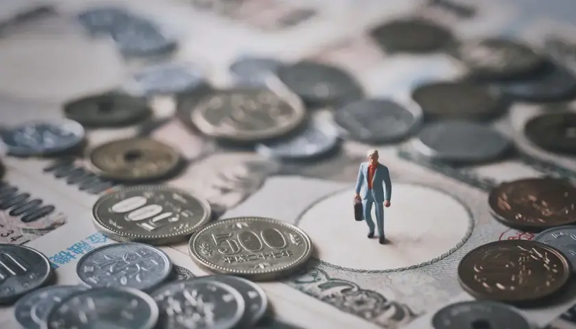 Mała figurka biznesmena stoi na tle japońskich banknotów i monet. To symboliczna wizja krajowej diety i finansów.