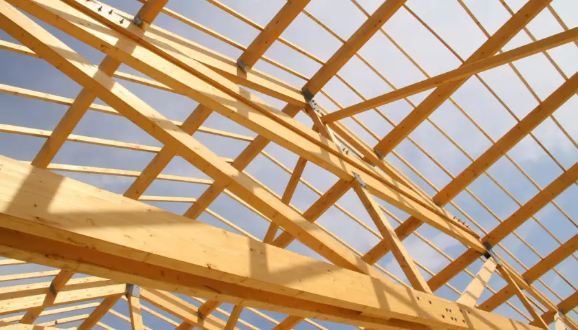Structure en bois d'une charpente, vue de dessous. Le ciel bleu et nuageux est visible à travers les poutres. Un aperçu pour estimer le prix charpente.