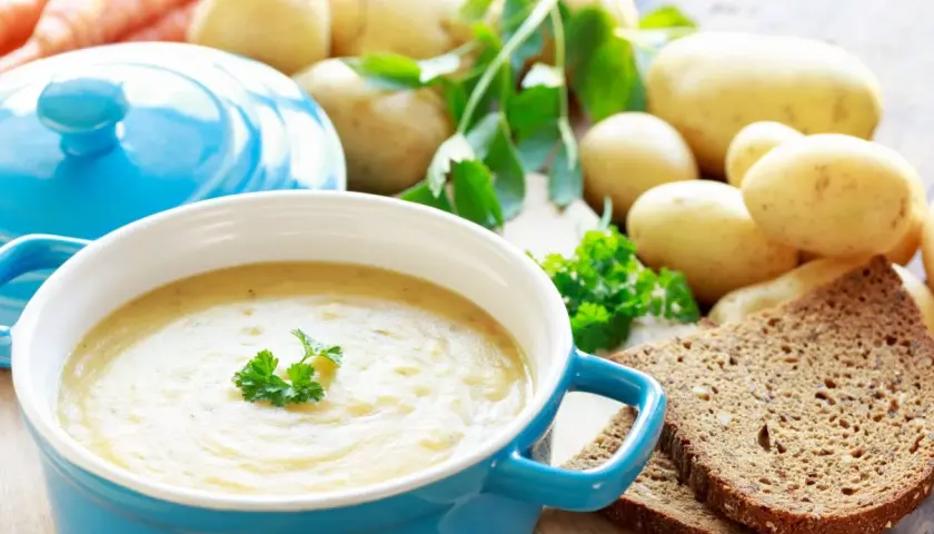 Pyszna zupa ziemniaczana przepis babci, podana w niebieskiej misce, z ziemniakami, marchewką i chlebem żytnim w tle.
