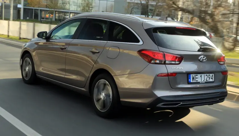 Szary Hyundai i30 1.6 CRDi kombi jedzie po drodze, widać jego tylną część i bok.
