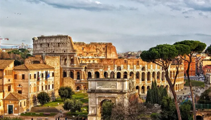 Colosseo e Arco di Tito, un'idea di cosa vedere a Roma in un giorno gratis, con pini romani e cielo nuvoloso.