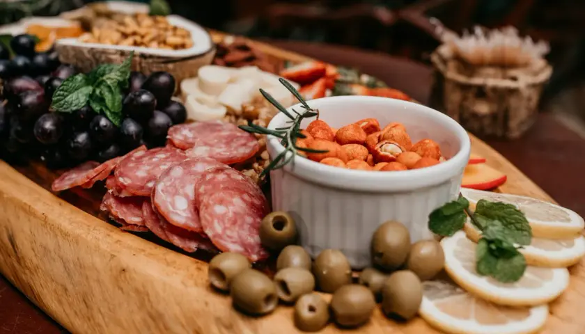 Un buffet campagnard pour 20 personnes : raisins noirs, salami, olives, cacahuètes épicées, citron et menthe sur un plateau en bois.