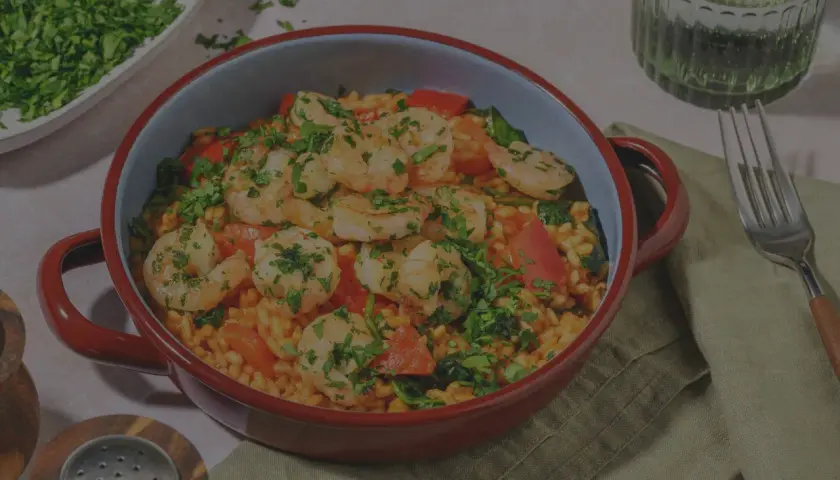 En härlig paella valenciana med saftiga räkor, paprika och ris, toppad med färsk persilja.