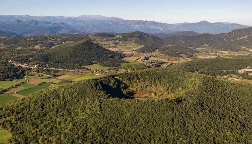 Paisaje aéreo de los volcanes de la Garrotxa, con conos volcánicos cubiertos de vegetación y un cráter visible.