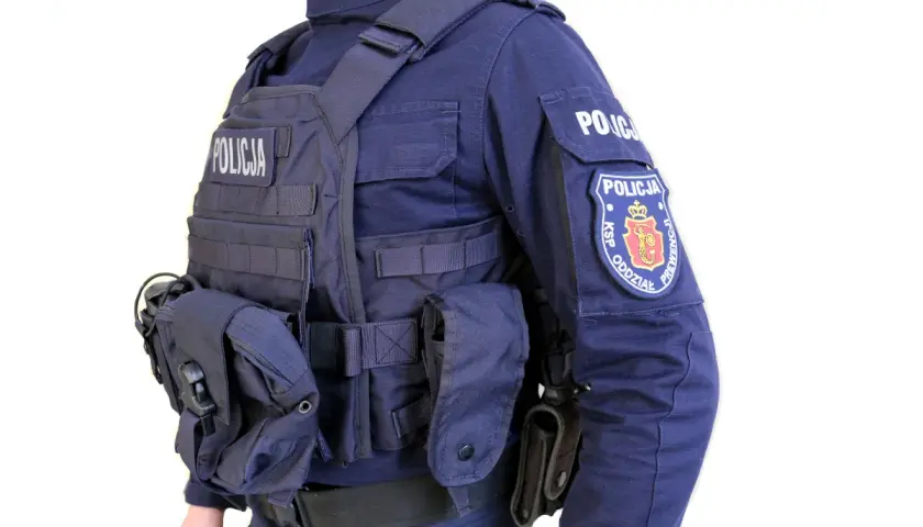 Policjant w pełnym rynsztunku, z kamizelką kuloodporną z napisem "POLICJA" i naszywką "KSP ODDZIAŁ PREWENCJI".