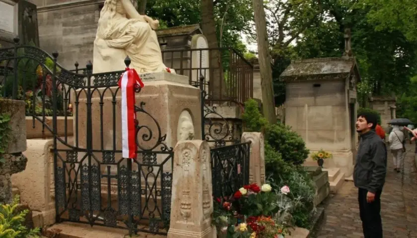 Pomnik na cmentarzu Père Lachaise z biało-czerwoną wstęgą. Mężczyzna wpatruje się w nagrobek.