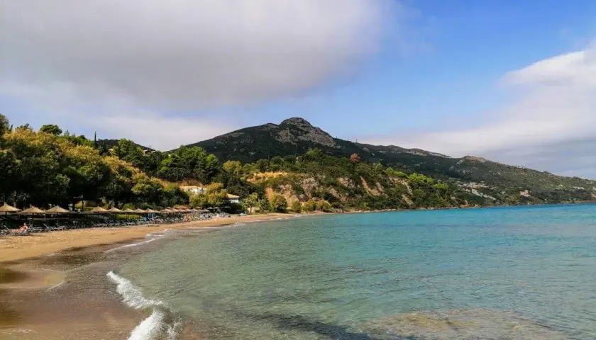 Piękna plaża Tragaki Zakynthos z turkusową wodą, zielonymi wzgórzami i rzędem leżaków pod parasolami.