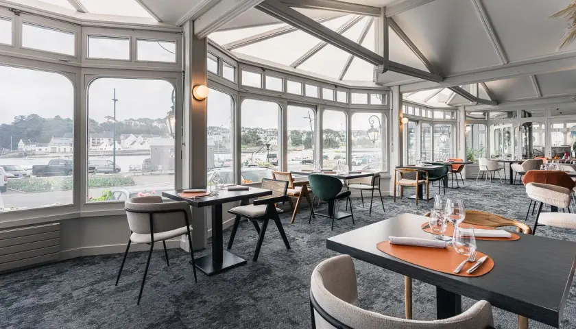 Salle de restaurant lumineuse avec vue sur le port, tables dressées et chaises modernes.