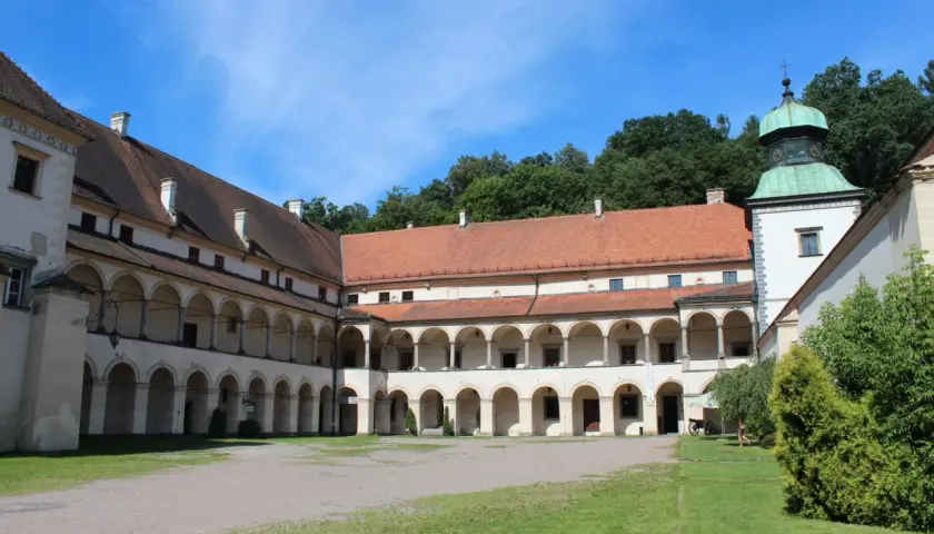 Dziedziniec zamku w Suchej Beskidzkiej z arkadowymi krużgankami i zieloną wieżą.