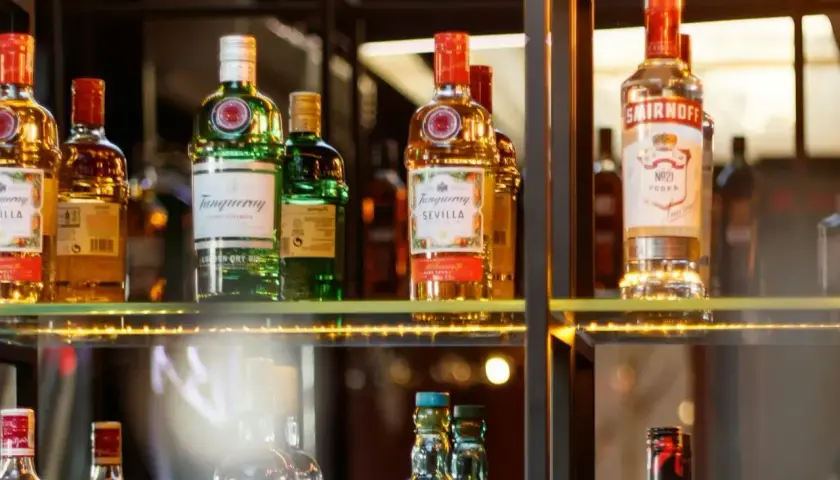 Butelki alkoholi na półce, w tym Tanqueray i Smirnoff. Idealne dla barmana na wesele, cena zależy od wyboru.
