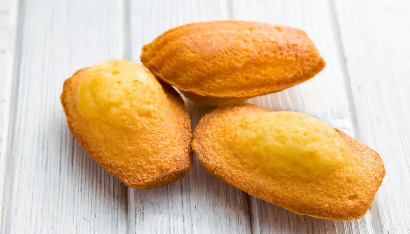 Trois madeleines dorées sur fond de bois clair, parfaites pour une recette de madeleines salées pour apéritif.