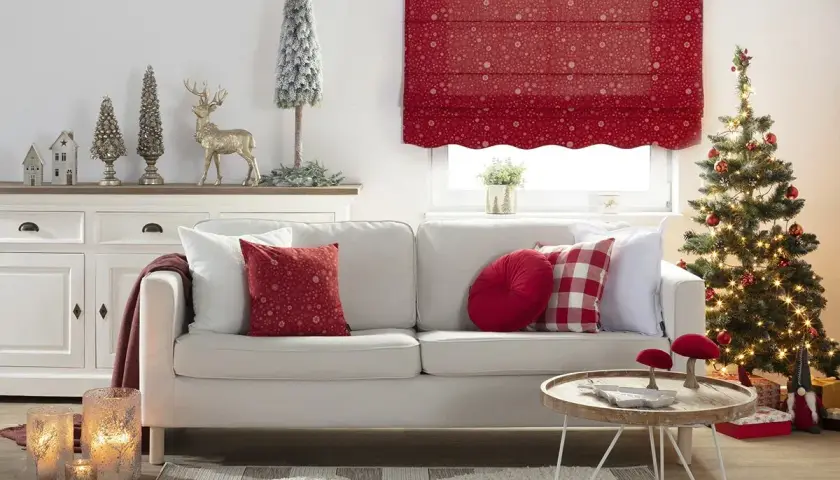 Przytulny, świąteczny salon z białą kanapą, choinką i ozdobami. Dominują akcenty w kolorze czerwonym, tworząc ciepłą atmosferę.