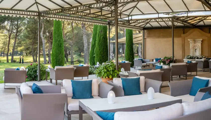 Terrasse de restaurant chic avec mobilier d'extérieur confortable et jardin verdoyant en arrière-plan.