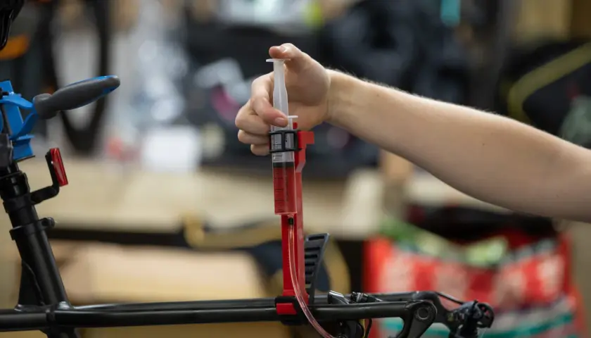 A hand uses a syringe filled with red fluid to bleed bicycle brakes. It's not as hard as you might think!