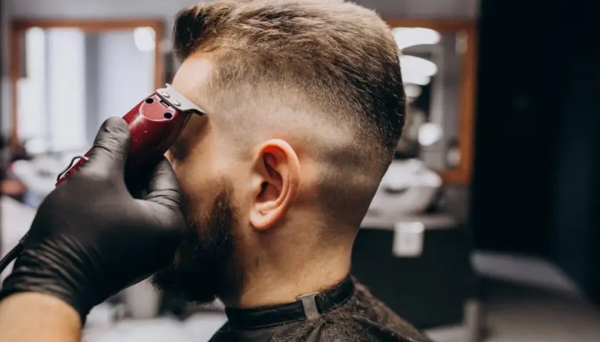 Barbero dando forma a un corte buzz cut fade con máquina. El cabello se desvanece suavemente de corto a largo.