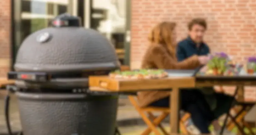 Un couple profite d'un repas en plein air avec une pizza sur une planche en bois à côté d'un barbecue kamado.