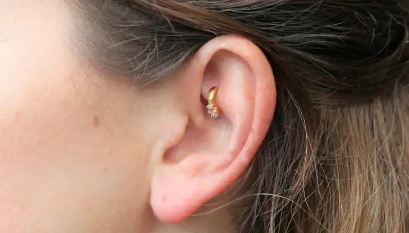 Złoty kolczyk w uchu, ozdobiony cyrkoniami, stanowi subtelny akcent. To modny rook piercing, który dodaje charakteru.
