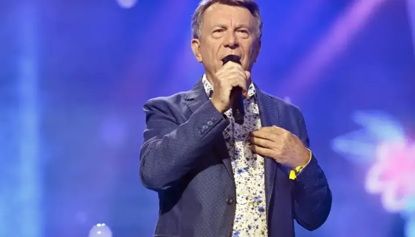 Wojciech Gąsowski w niebieskiej marynarce i kwiecistej koszuli śpiewa na scenie.