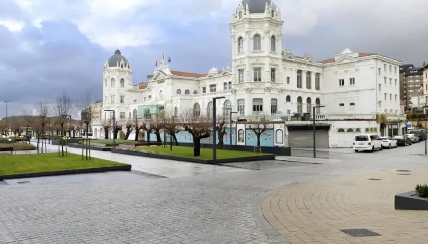 Edificio blanco con cúpulas en la plaza Italia Santander. Árboles desnudos y césped verde.