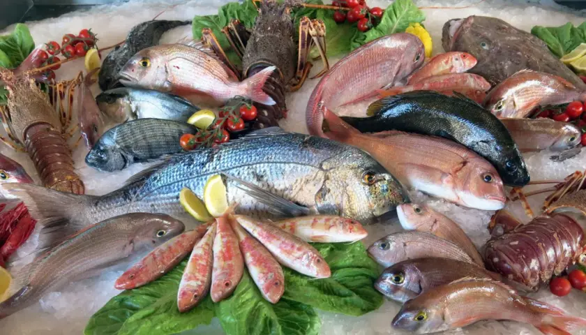 Un banco di pesce fresco su ghiaccio: aragoste, orate, triglie e un magnifico pesce azzurro al centro.