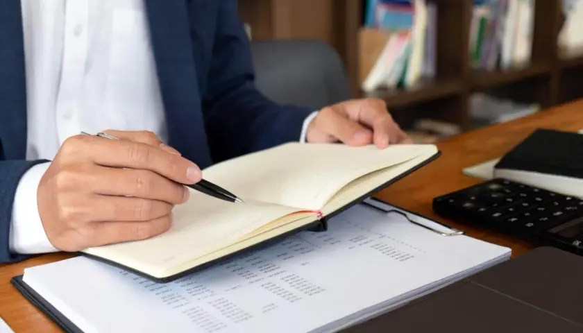Mężczyzna w garniturze notuje w dzienniku, analizując dokumenty. Szybki odpis księgi wieczystej online ułatwia pracę.