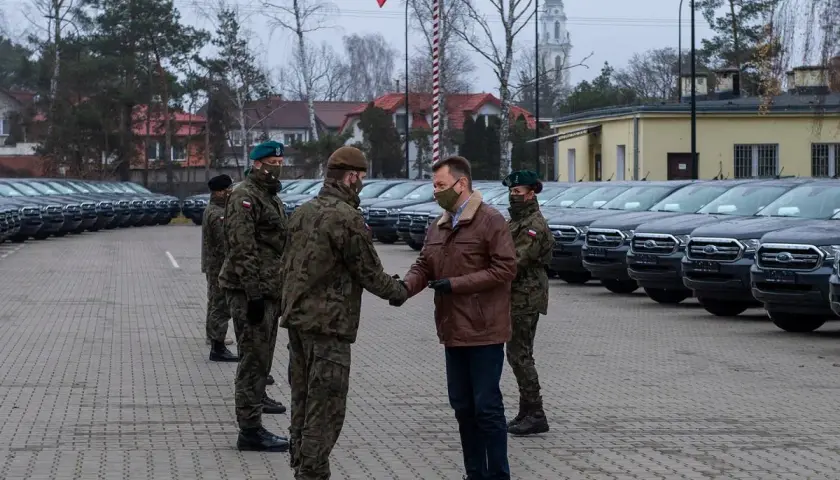Rangers wojsko odbierają nowe pojazdy. W tle rzędy samochodów i polska flaga.