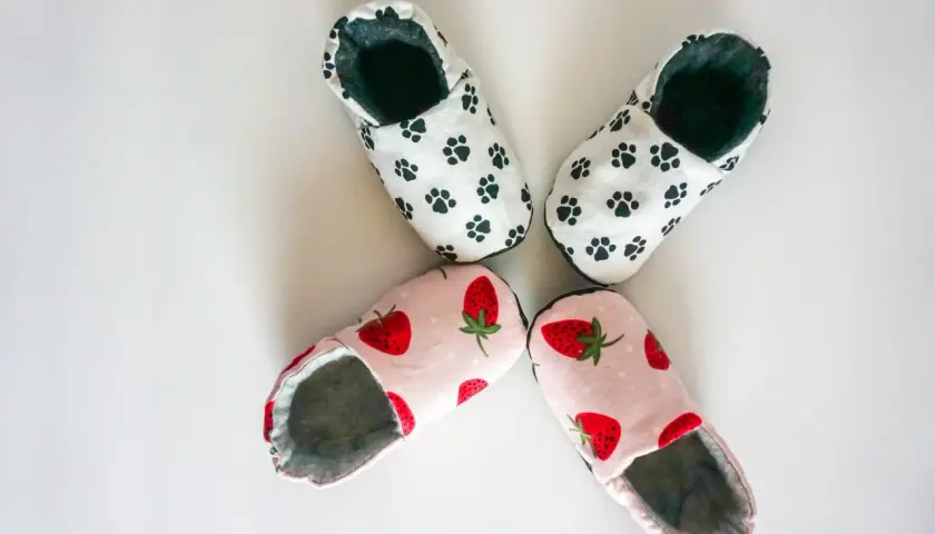 Zwei Paar süße Babyschuhe: eins mit Pfotenabdrücken, eins mit Erdbeeren. Hier findest du ein schnittmuster babyschuhe kostenlos zum Nachnähen!