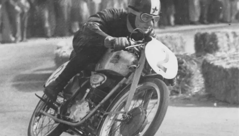 El piloto de carreras Carlo Ubbiali inclinado en su moto con el número 2, compitiendo con determinación.