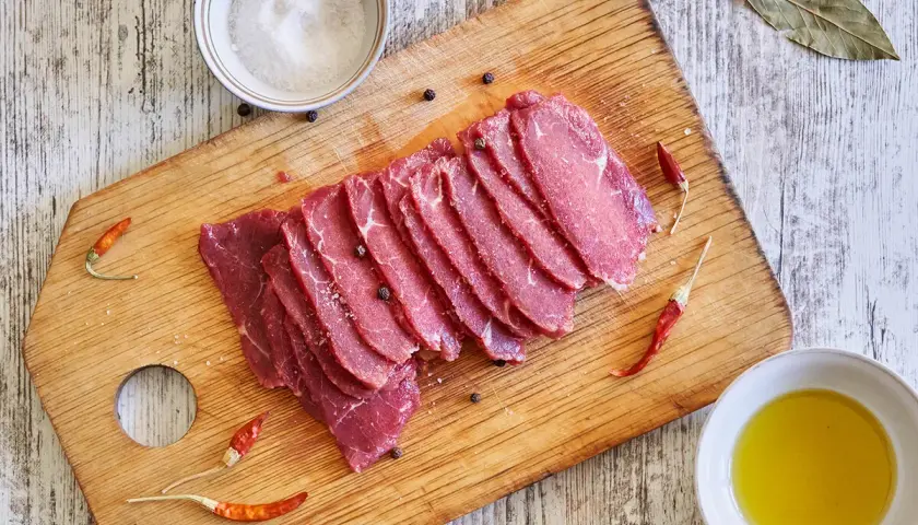 Filete de ternera crudo, cortado en finas lonchas, sobre tabla de madera con sal, pimienta, guindillas y aceite de oliva.