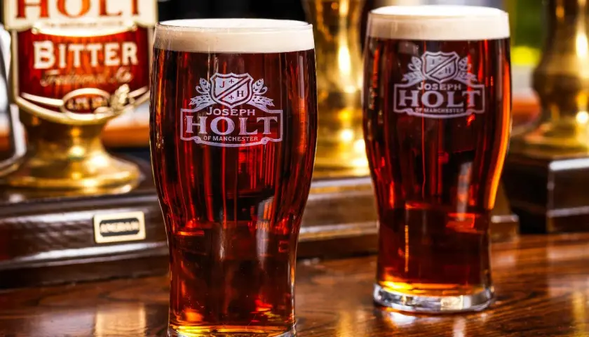 Deux verres de bière ambrée, une cask ale Joseph Holt, sur un comptoir en bois.