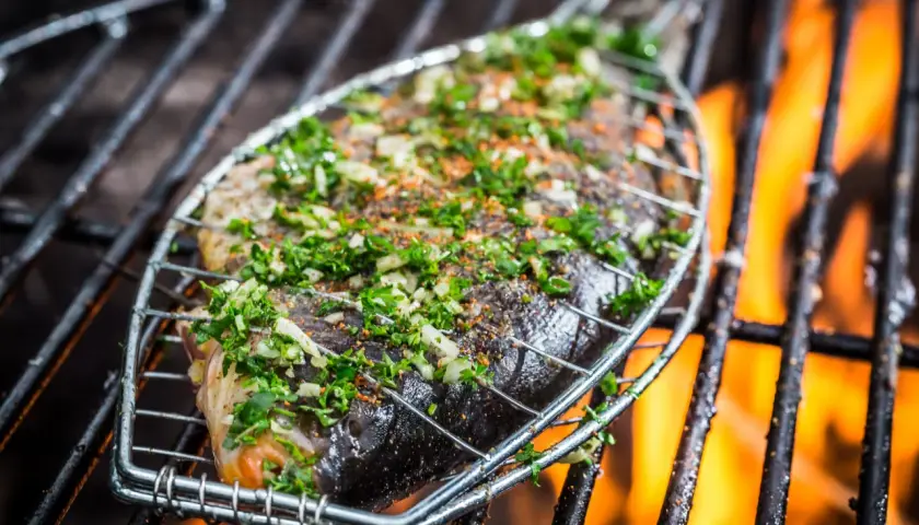 Poisson entier assaisonné d'herbes et d'épices, sur une grille de barbecue avec des flammes vives. Le temps de cuisson du poisson au barbecue est crucial pour un résultat parfait.